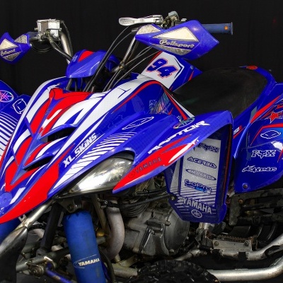 Quadro todo-terreno azul, vermelho e branco com autocolantes e texto YAMAHA, 94, RAT, em fundo escuro