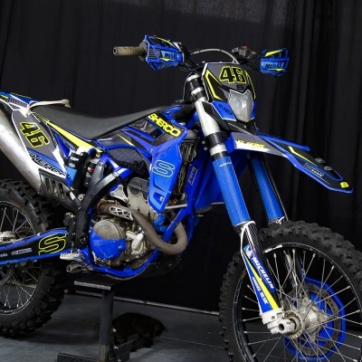 Moto de enduro azul com números amarelos e pneus de lama