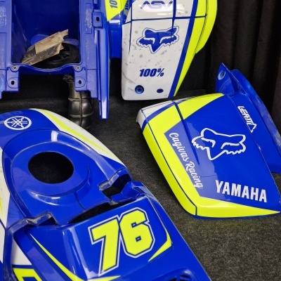 Peças para mota Yamaha azul, amarelo e branco com número 76 e logos diversas