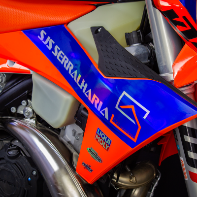 Detalhe lateral de mota KTM vermelha e azul com texto SIS SERRALHARIA