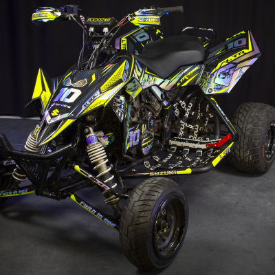 Quad Suzuki preto e amarelo com decoração roxa, pneus largos e assento preto, em fundo preto