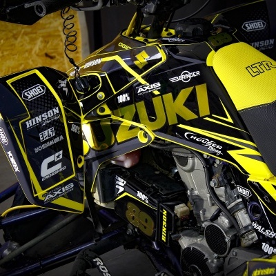 Quad Suzuki amarelo e preto com vários logotipos e números visíveis.