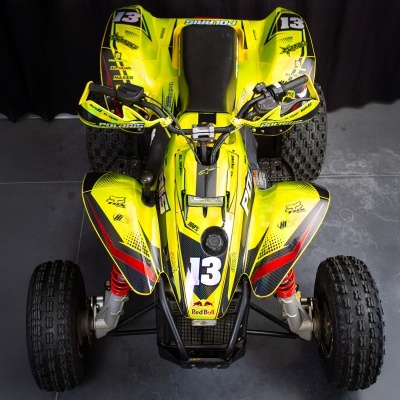 Quadriciclo amarelo com detalhes vermelhos e pretos sobre piso cinzento