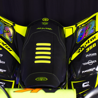 Assento de mota preto com detalhes amarelos, azuis e roxos e texto Raptor 350 e 82