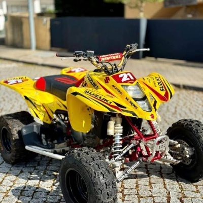 Quadriciclo Suzuki amarelo e vermelho com pneus grandes estacionado numa calçada portuguesa