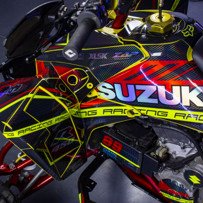 Quadro de competição Suzuki com detalhes em vermelho, amarelo e preto, texto SUZUKI e RACING visíveis.
