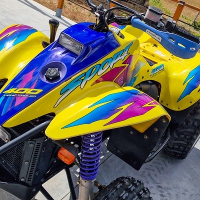 Quad amarelo e azul com detalhes roxos e rosas em piso de cimento próximo a cerca de madeira