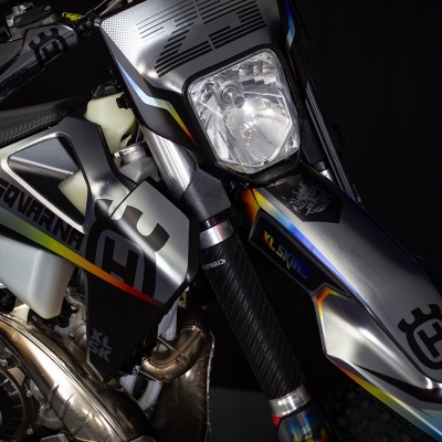 Motocicleta Husqvarna preta, cinza, azul e amarelo com farol quadrado e logótipo