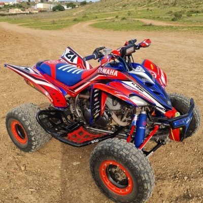 Quad Yamaha azul, vermelho e branco com pneus grossos em terreno de terra batida