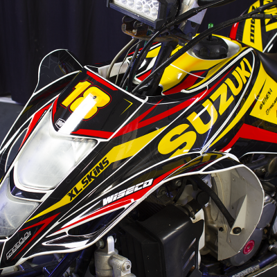 Quadra Suzuki preta, amarela e vermelha com número 18 e várias marcas visíveis.