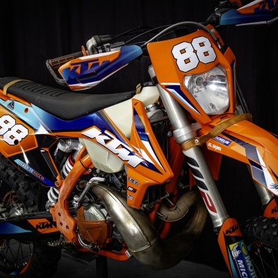 Motociclo todo-o-terreno KTM laranja com número 88 branco, detalhes azuis e brancos, pneus de rasto