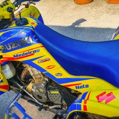 Moto Suzuki azul e amarelo com autocolantes diversos em piso de cimento