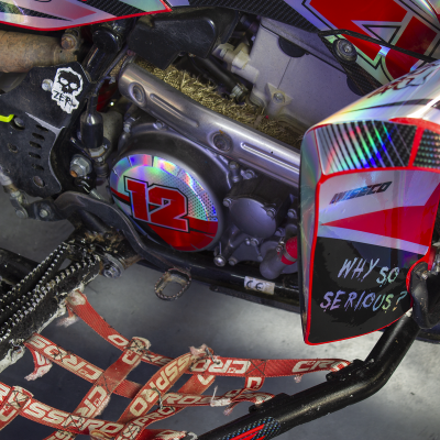 Close-up de parte de kart com chassis preto, corrente, assento com cinto vermelho e decalques coloridos.