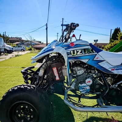 Quad Suzuki azul e branco em relvado sob céu limpo