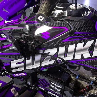 Parte lateral de motocicleta Suzuki preta e roxa com detalhes em fibra de carbono e texto visível