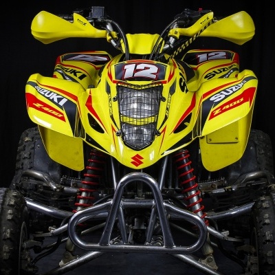 Quadriciclo amarelo com números 12 e marca SUZUKI, fundo preto.