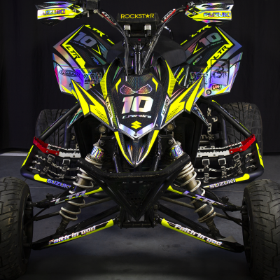 Quadriciclo de corrida com cores amarelo, preto e azul, pneus lisos e diversos adesivos em fundo escuro