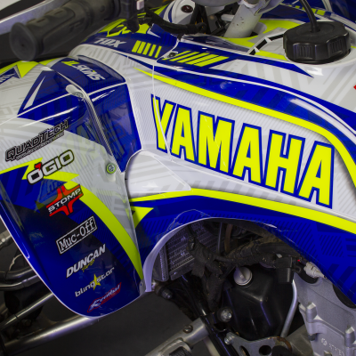 Moto todo-o-terreno Yamaha azul, branco e amarelo com várias etiquetas de marcas