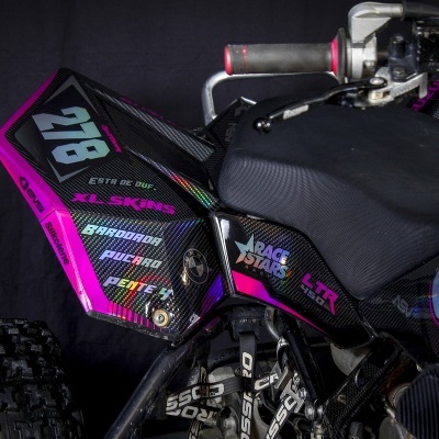 Mota de todo-o-terreno com fibra de carbono preta e detalhes rosa, número 278 e várias etiquetas coloridas.