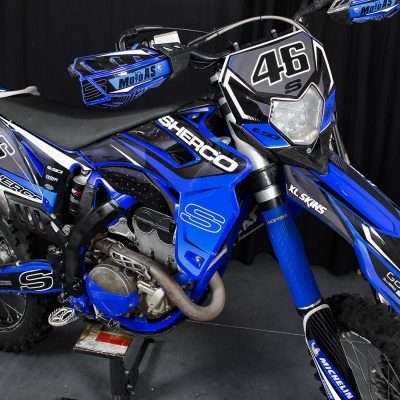 Motocicleta de corrida azul e preta Sherco com números 46 e marcas visíveis