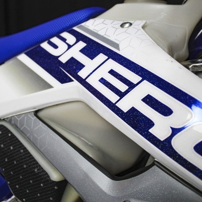 Parte lateral branca e azul metálico de uma moto com texto SHERCO