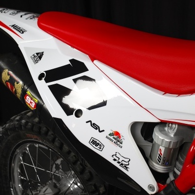 Parte traseira de moto de motocross com banco vermelho e autocolantes visíveis