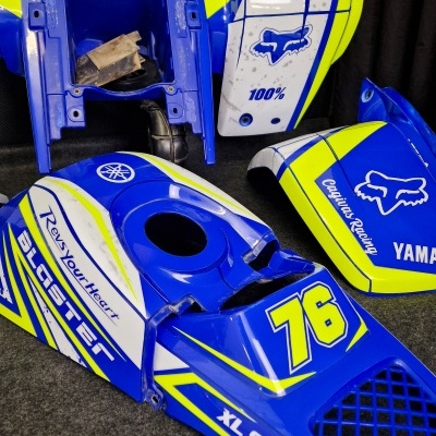 Peças de moto azuis, brancas e amarelas com números 76 e várias marcas visíveis.