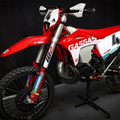 Motocross GASGAS vermelha e branca com número 4 apoiada em suporte.