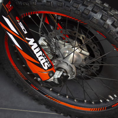 Roda de mota todo-o-terreno com pneu cravado e garfo preto com adesivo Mitas