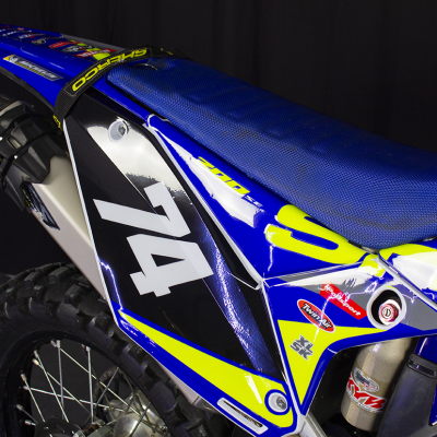 Moto azul de motocross com número 74 e autocolantes visíveis.