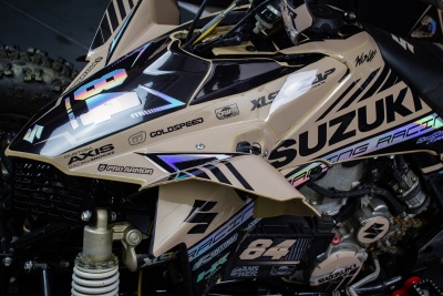 Quadri moto Suzuki creme com detalhes em preto e azul, número 84 e várias inscrições de marcas.