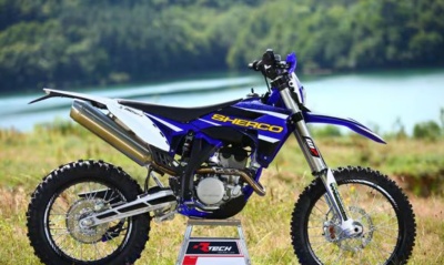 Motocross azul SHERCO em ambiente exterior com vegetação e água.