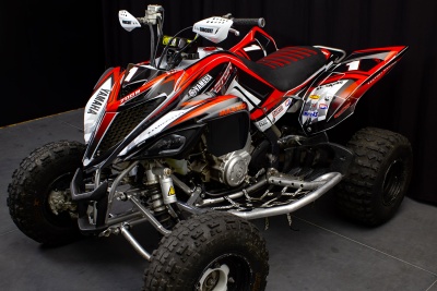 Quad Yamaha vermelho, preto e branco com texto YAMAHA e RAPTOR sobre fundo preto