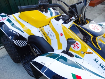 Quadriciclo branco com detalhes em amarelo, preto e verde, banco amarelo e etiquetas com texto e símbolos