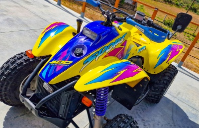 Quadriciclo amarelo colorido com texto 400 Liquid Cooled e Sport estacionado em calçada de cimento