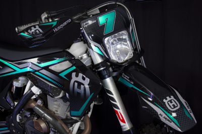 Motociclo off-road preto com detalhes em azul-turquesa e cinzento e o número 7