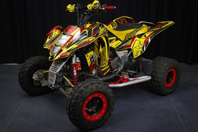 Quadriciclo amarelo com detalhes em vermelho e preto, pneus largos, suspensão vermelha e guiador com proteção