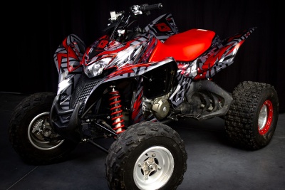 Quad ATV vermelho e preto com padrões abstratos e pneus grandes em fundo escuro