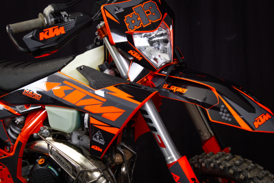 Motocross KTM laranja, preto e cinzento, número #13, etiquetas visíveis em fundo escuro
