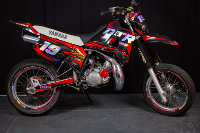 Motociclo Yamaha DT vermelho, preto e branco com números 19 em fundo escuro