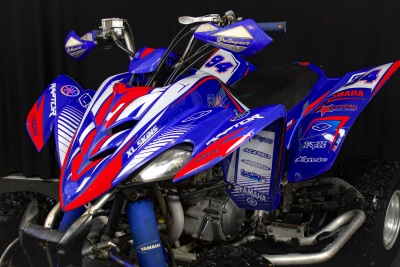 Quadro todo-terreno azul, vermelho e branco com autocolantes e texto YAMAHA, 94, RAT, em fundo escuro