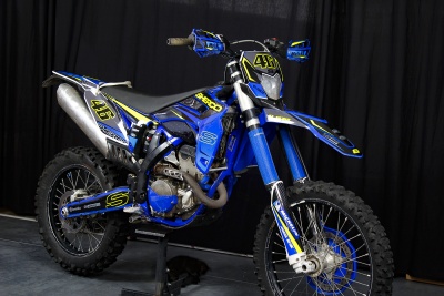 Moto de enduro azul com números amarelos e pneus de lama