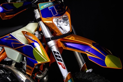 Motocross KTM colorida com números e marcas visíveis, em fundo preto