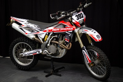 Motocross Husqvarna branca, vermelha e preta com número 392 em suporte
