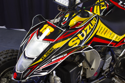 Quadra Suzuki preta, amarela e vermelha com número 18 e várias marcas visíveis.