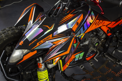 Quadro todo-o-terreno preto com detalhes em laranja, amarelo, roxo e adesivos visíveis