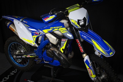 Motocross Sherco 300 SE azul, branco e amarelo com autocolantes e pneus de trilha sobre fundo negro