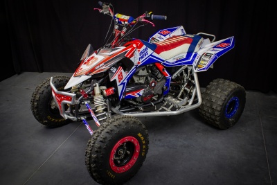 Quadriciclo branco, vermelho e azul sobre piso cinzento, fundo preto