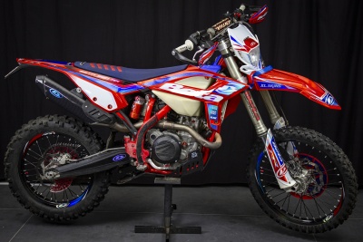 Motocross vermelho, azul e branco com pneus cravados e suporte preto.