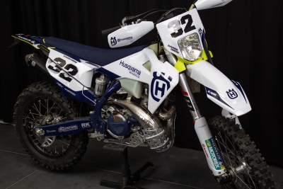 Motocross Husqvarna branca, azul e amarela com números 32 em fundo preto